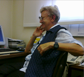 Maria Maddalena Novati with short hair and glasses, smiling, sits at a desk with a computer and phone.