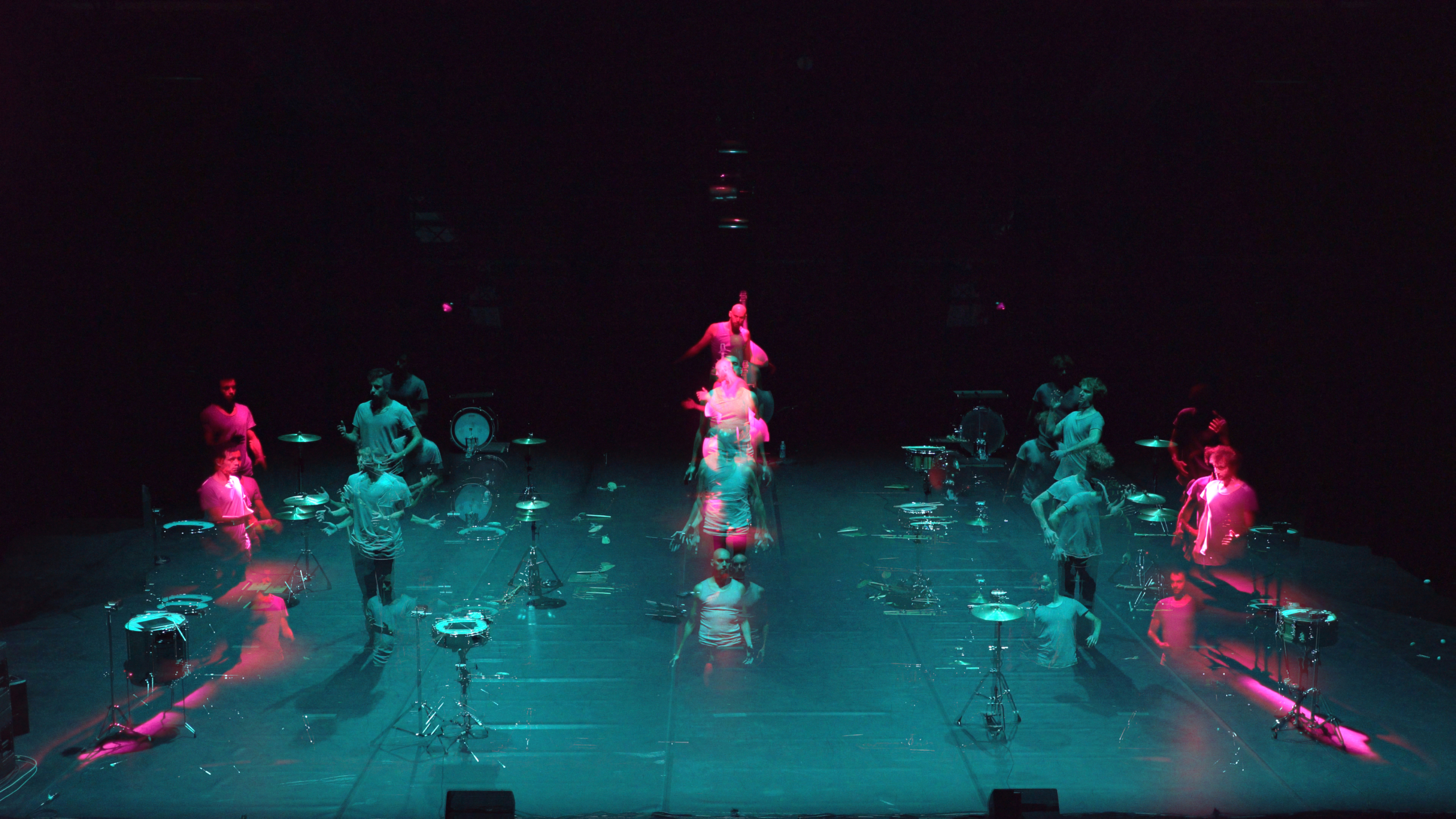 Photograph of a music production on a stage, dramatized in colored lighting and with musicians multiplied in different states of motion.