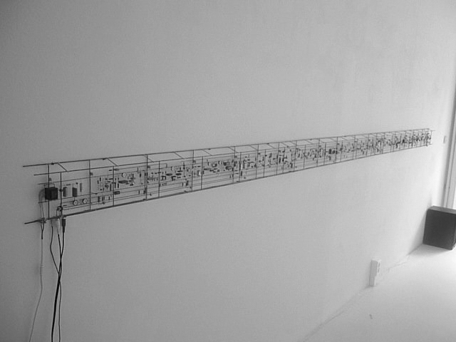 A minimalist, monochromatic wall installation features a long, narrow circuit-like structure with intricate components.
