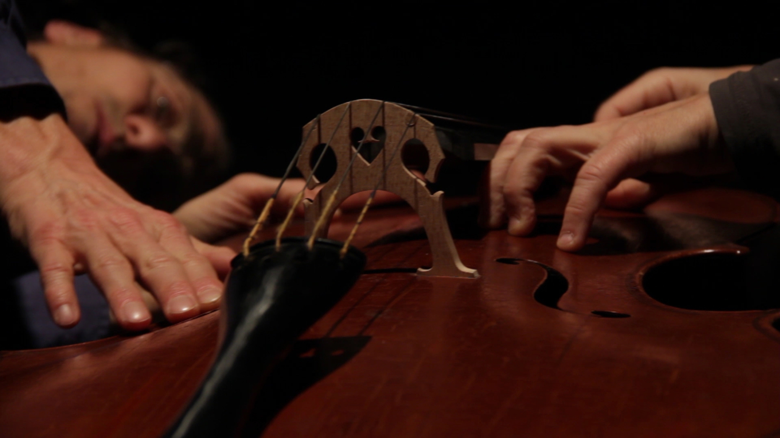Two hands gently touch a cello, capturing a moment of intimate interaction with the instrument.