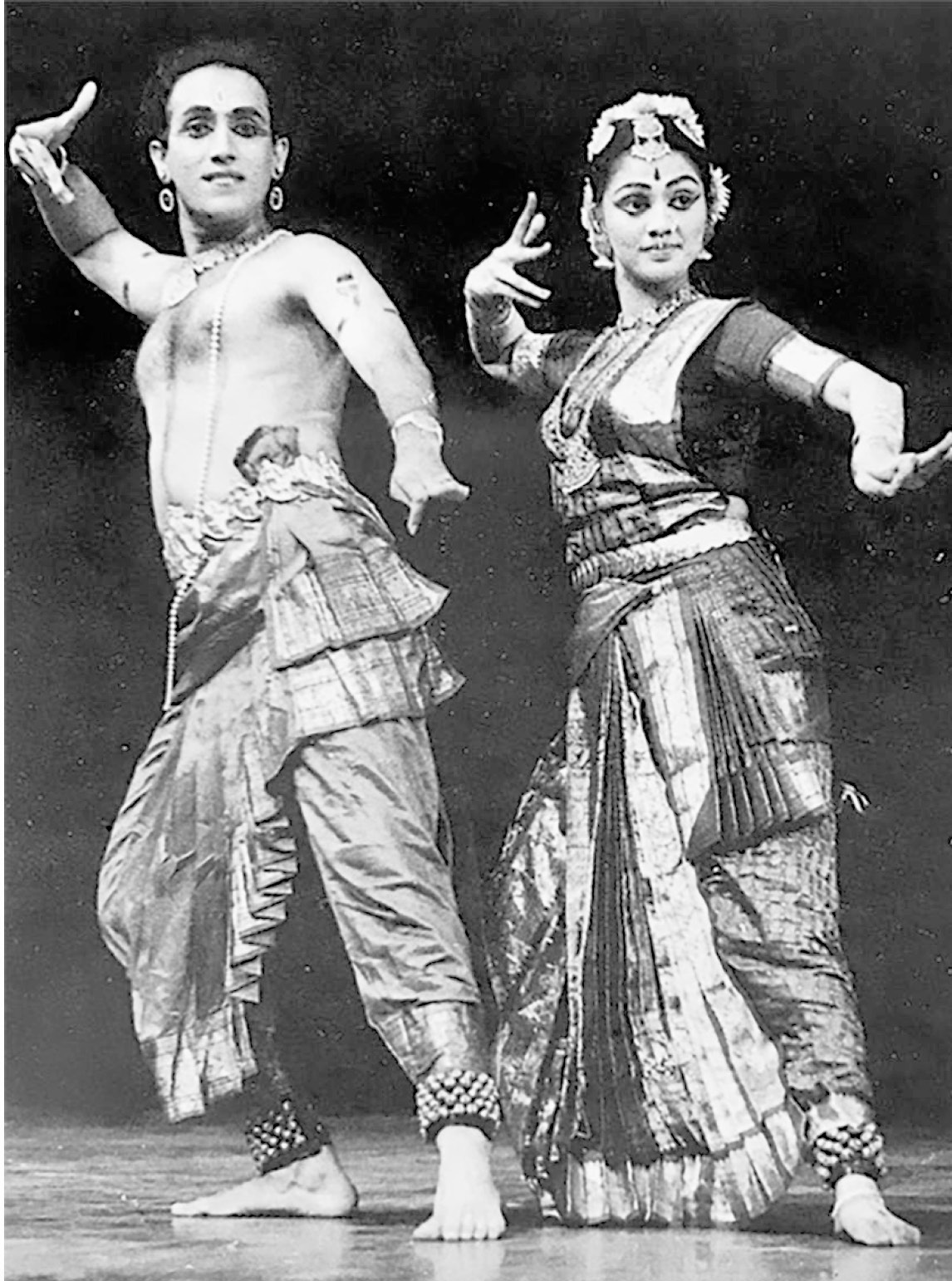 Black and white foto of two persons, one in traditional female, one in traditonal male Indian dress, in a synchronous position from traditional Indian dance.