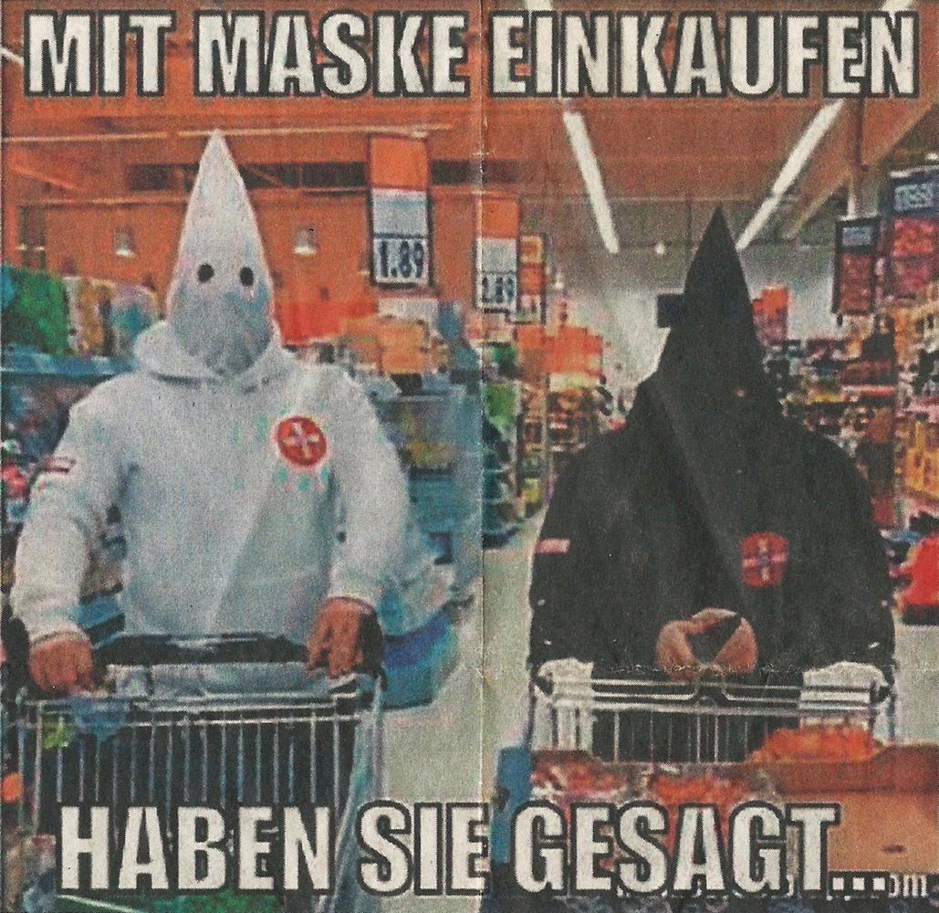 A color photo shows two people in Ku Klux Klan-like masks standing with shopping carts in a supermarket. One is dressed entirely in white, the other entirely in black. Above it, in meme format, large letters read: “Shopping with a mask, they said …”.