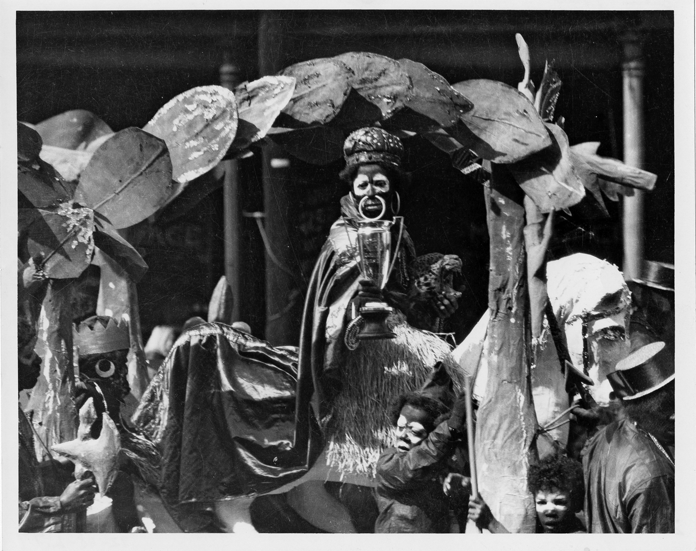 Ein Schwarzweißfoto vom Straßenkarneval zeigt kostümierte Leute in Blackface – unter anderem eine Person mit Krone und Umhang.