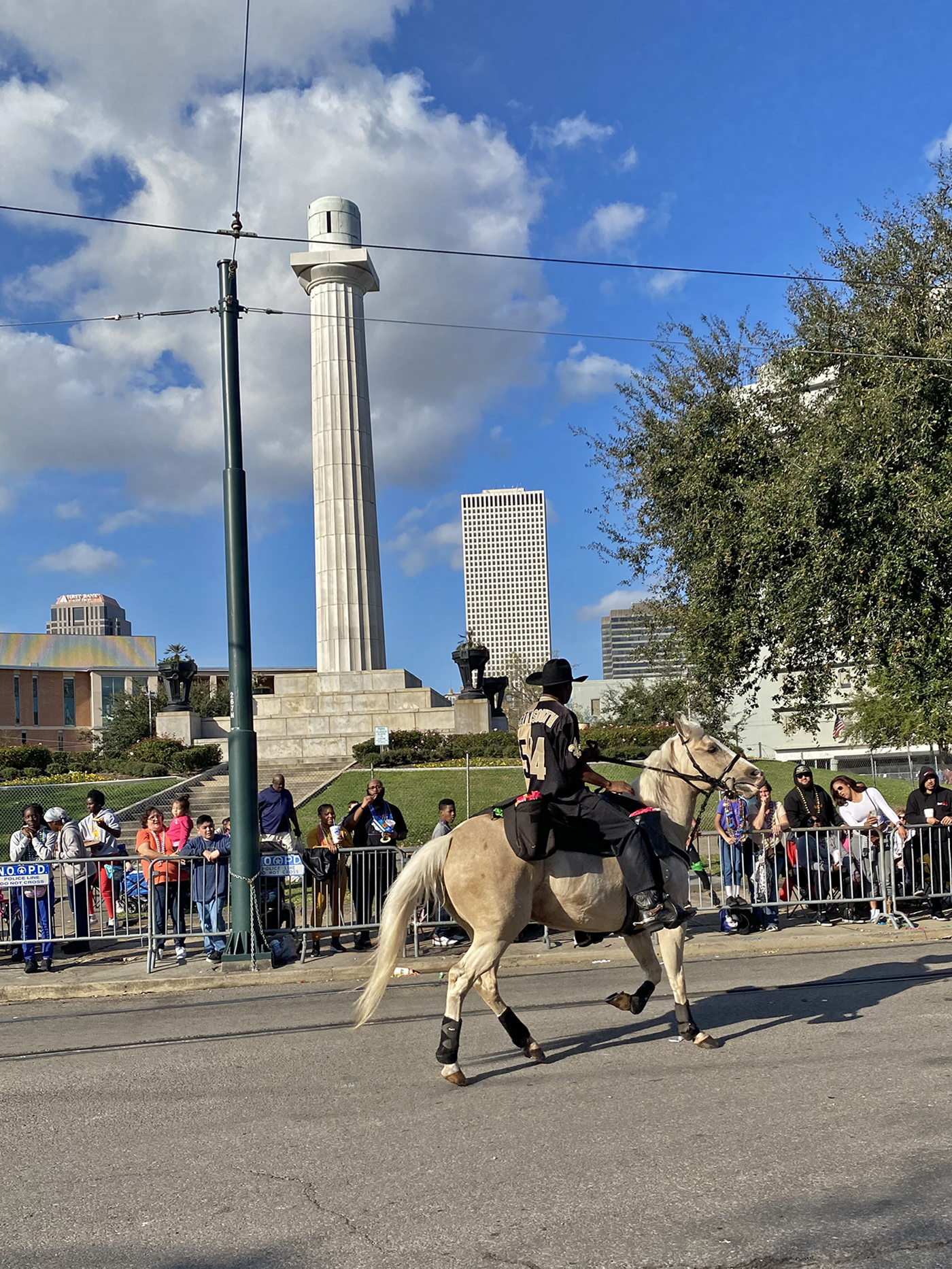 Ein Farbfoto zeigt einen leeren Denkmalsockel; davor reitet jemand auf einem hellen Pferd. Hinter Absperrungen sind Zuschauende zu sehen.