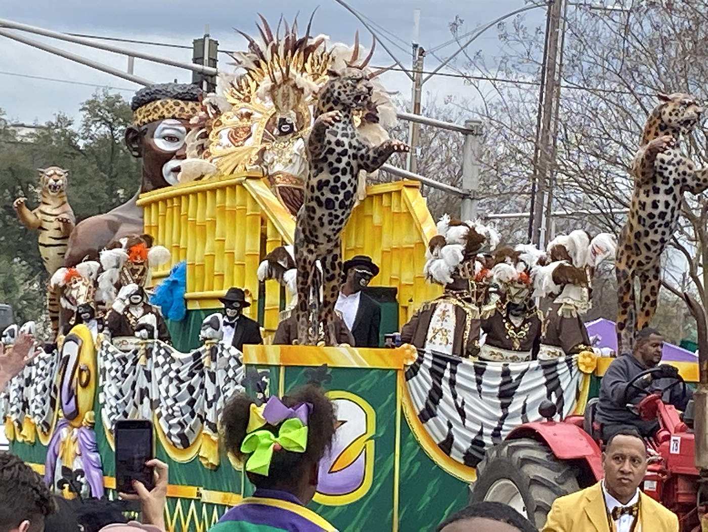 Ein Farbfoto zeigt einen Karnevalswagen, auf dem kostümierte Leute in Blackface und zum Teil mit Kopfschmuck aus Federn, zwei Leopardenfiguren sowie eine überlebensgroße Figur in Blackface und mit Leopardenstirnband zu sehen sind.