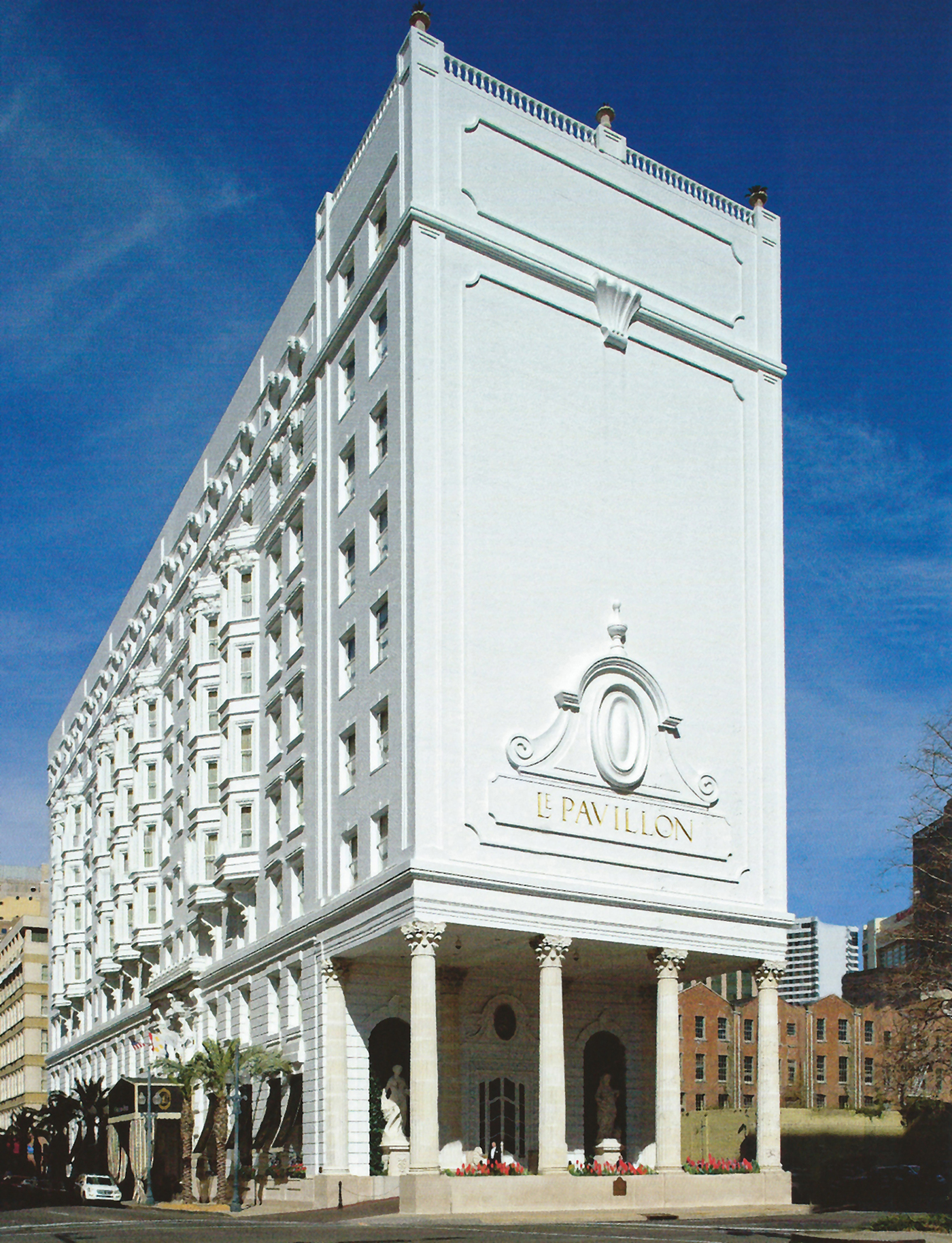Ein Farbfoto zeigt eine weiße Hausfassade mit Stuck, vier Säulen, zwei Statuen und der Inschrift 