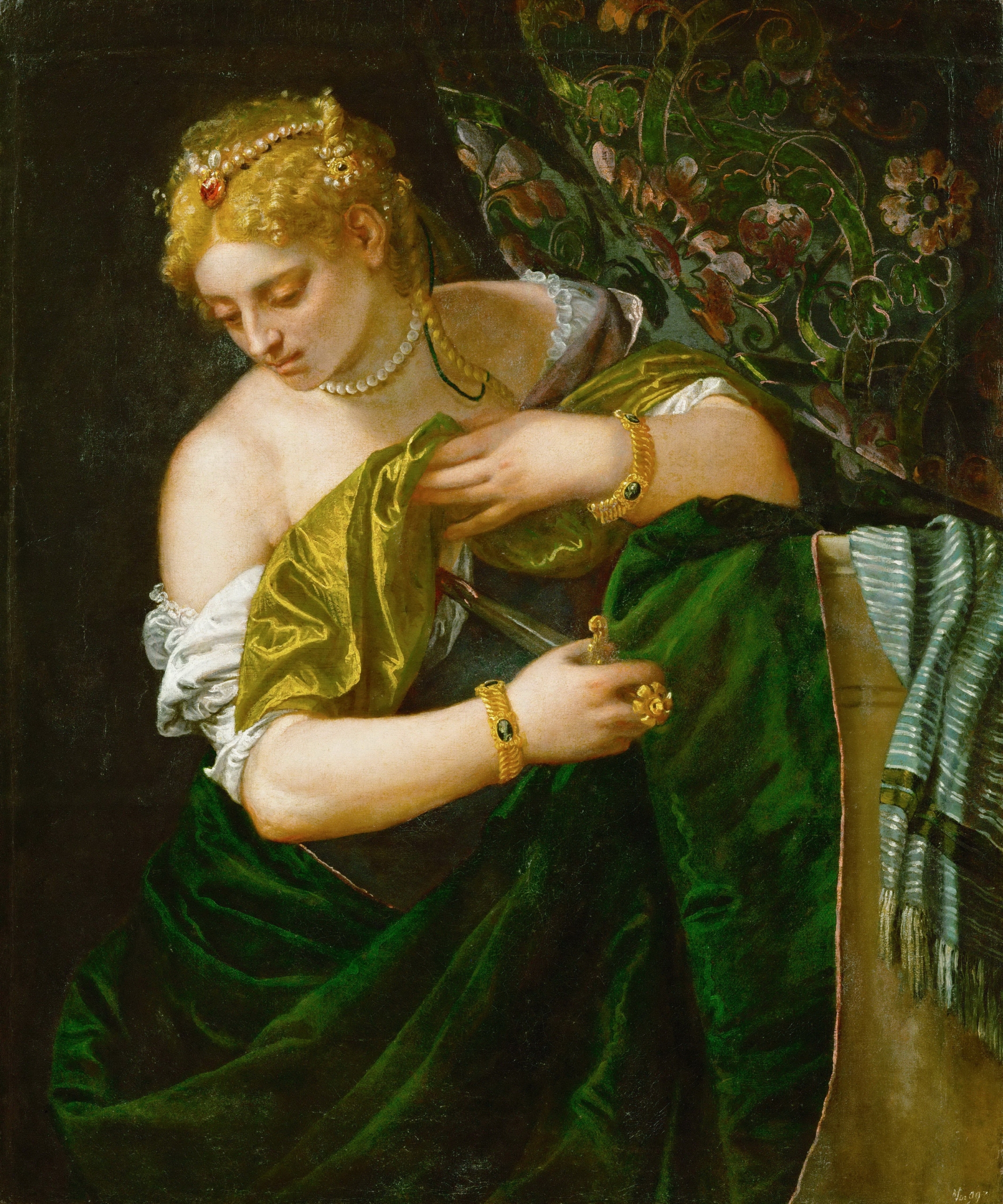 A Renaissance painting of a woman in luxurious green and gold garments, adorned with pearls and jewellery. She looks downward while holding a small object in her hand, her expression contemplative. The rich fabrics and detailed textures highlight the artist’s mastery of light and colour.