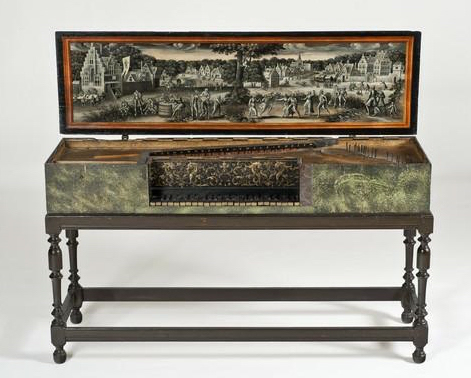 Virginal on a dark wooden stand, featuring an open lid decorated with a detailed painting in muted tones. The artwork inside the lid depicts a lively village scene with elegantly dressed figures, musicians, and dancers set among trees and tall gabled buildings. The instrument’s exterior has a mottled green finish with subtle decorative texture, while the keyboard area shows intricate floral patterns around the keys. The instrument combines refined craftsmanship with artistic decoration, typical of early Baroque European design.