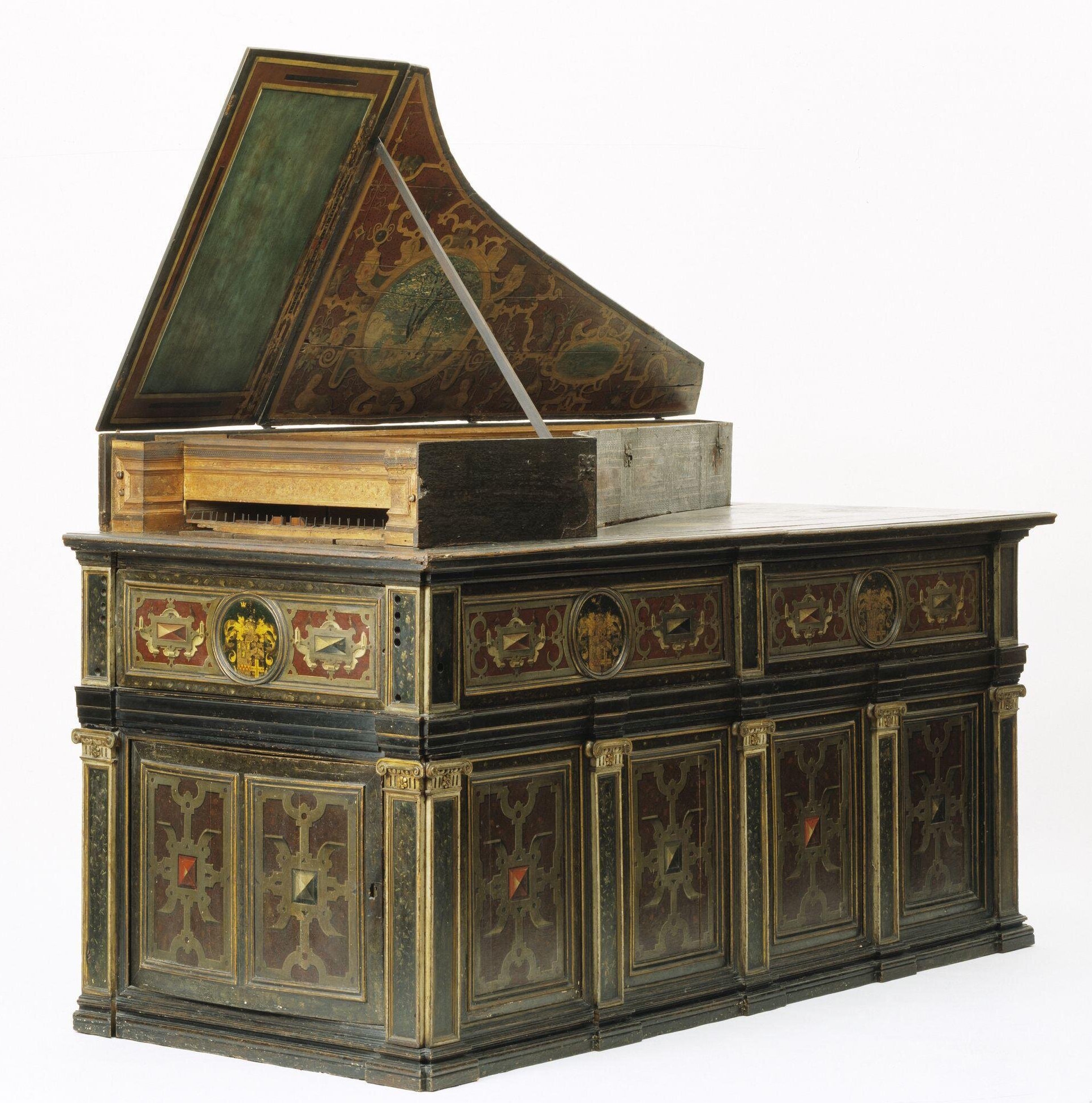 Claviorgan with an ornate wooden case and a partially open lid revealing decorative painted panels. The instrument is set atop an elaborately crafted cabinet base featuring geometric inlays, gilded accents, and intricate paneling in red, green, and gold tones. The harpsichord’s lid interior displays a painted design with floral and heraldic motifs, while the keyboard area remains plain wood, highlighting contrast between simplicity and luxury. The structure exemplifies high-level craftsmanship from the 16th or 17th century, merging musical function with fine furniture artistry.