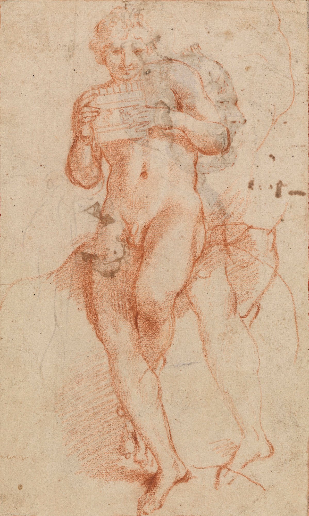 A red chalk drawing depicting Bacchus as a youthful male figure, standing and playing a set of panpipes. The figure is nude, rendered with soft shading and fluid lines, conveying a sense of gentle movement. Behind him, faint sketch lines suggest an earlier or alternative pose.