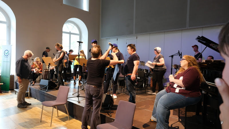 Foto von vielen Personen / Musikern auf der Bühne beim Soundcheck bzw. Aufbau. 