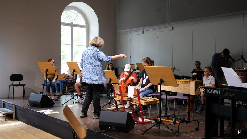 Foto von acht musizierenden Kindern und einer Dirigentin