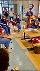 Foto von einer Gruppe von musizierenden Frauen, die in einem Kreis sitzten: gespielte Instrumente sind Geige, zwei Gitarren, Kontrabass und Percussioninstrumente. 