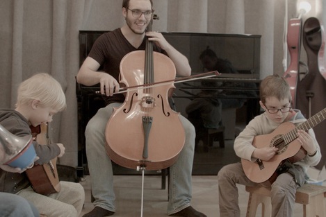 Student spielt Cello, rechts und links von ihm sitzen zwei Jungs und spielen auf Gitarren