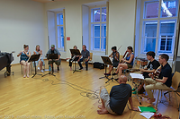 Foto mit 10 Musikern die in einem Halbkreis sitzen und gemeinsam musizieren