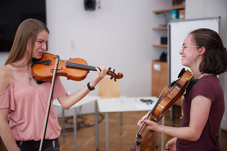 Zwei Studentinnen die sich gegenüberstehen und Geige spielen. 