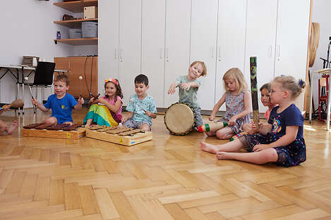 Am Boden sitzende Kinder die mit Schlaginstrumenten musizieren. 