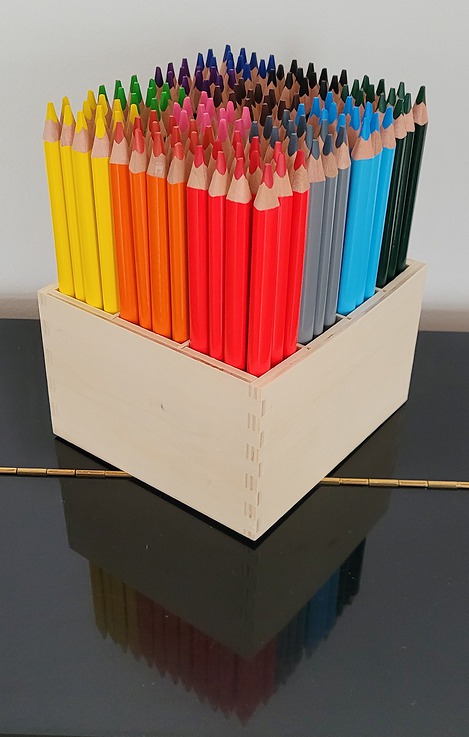 Holzbox mit Buntstiften in diversen Farben auf einem Klavier 