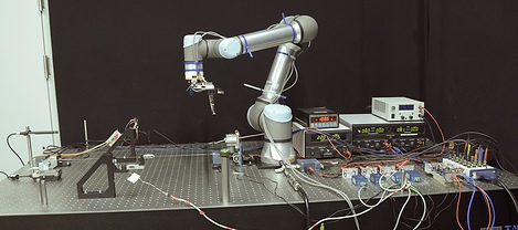 The experimental setup at the IWK laboratory. A cello string is mounted on a vibration-isolated optical table, with the UR5e robotic arm positioned for bowing. Force sensors at the string terminations and on the bow measure vibration and contact force simultaneously