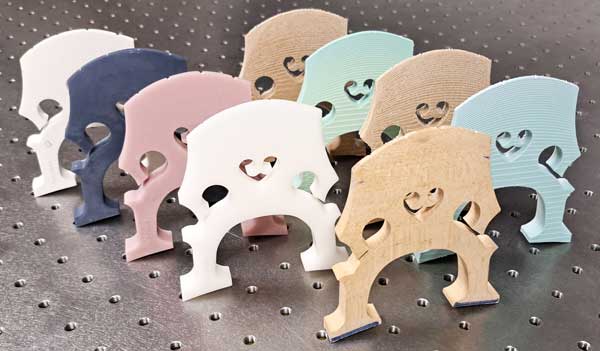 9 cello bridges standing on an optical table: one wooden, 4 FDM and 4 MSLA 3d printed versions