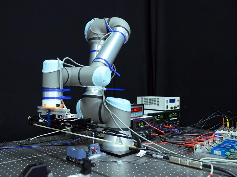 robotic arm mounted on an optical table holding a cello bow exciting a single string mounted on that table attached using sensors