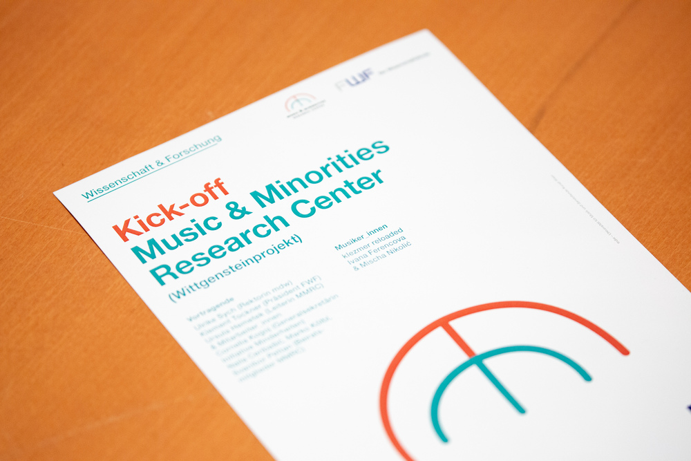 Veranstaltungsflyer, der das Logo des MMRC zeigt, das ein stilisiertes rostrotes "m" über einem türkisen "m" zeigt, darunter in Schwarz der Schriftzug  "Music & Minorities Research Center"